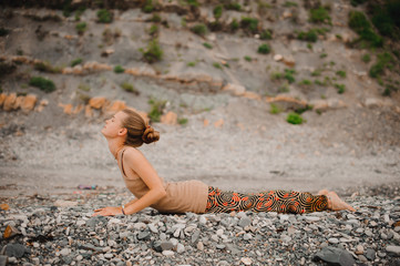 Young woman doing yoga on a rocky seashore. upward facing dog pose