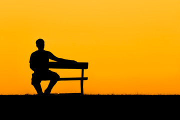 Fototapeta na wymiar A silhouette of man sitting on bench in sunset
