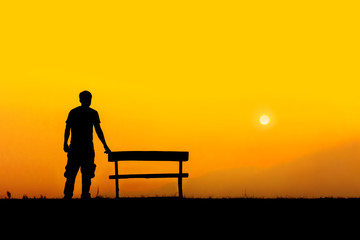 Fototapeta na wymiar A silhouette of man standing with bench