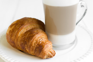 Croissant and glass of latte coffee on white plate