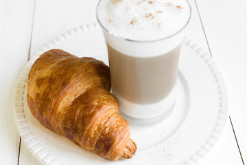Croissant and glass of latte macchiato on white plate