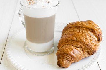 Croissant and glass of cafe latte on white plate