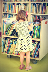 Little girl is choosing a book in the library.