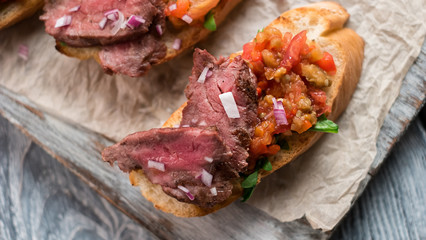 Piece of meat on sandwich. Sliced baguette and vegetables. Bruschetta with veal and onion. Healthy food in italian cafe.