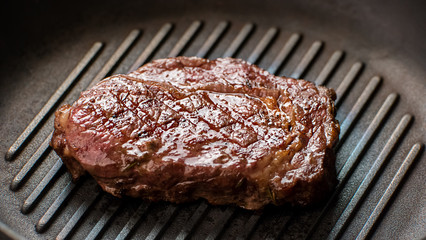 Meat on frying pan. Dark-colored piece of meat. Ribey steak cooked at restaurant. Delicious juicy beef.