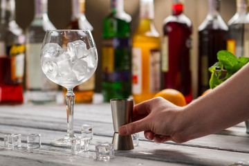 Wineglass with ice and jigger. Male hand with bar jigger. Tool of bartender. Choose ingredients for your cocktail.