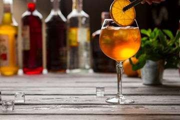 Wineglass with orange drink. Tongs hold slice of orange. Aperol spritz served at bar. Soda water and sparkling wine.