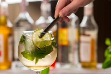 Tongs hold slice of lime. Mint leaves in beverage. Sweet syrup and sour juice. Chilled hugo...