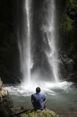 Man sitting in front of the spray of a waterfall