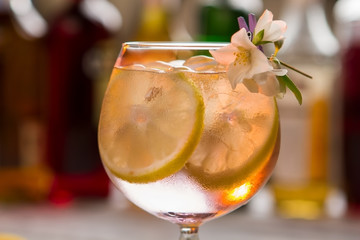 Cocktail with lemon slice. Ice and small flower. Tom collins served at bar. Gin and carbonated water.