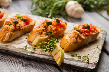 Piece of lemon and toasts. Small capers and fish meat. Bruschetta with baked salmon. Dish from italian cuisine.