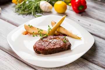 Plate with piece of meat. Sliced pear and herb. Freshly cooked ribeye steak. Tasty dish served with fruit.