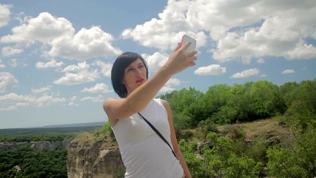 Attractive woman make selfie on smartphone on a background of mountains