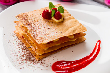 Dessert with sauce on plate. Raspberries and mint leaves. Sweet taste of millefeuille. Crispy pastry with custard.