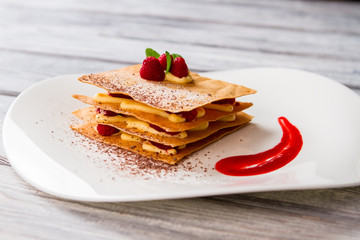 Dessert with yellow custard. Berries and chocolate powder. New recipe of raspberry millefeuille. Smear of fruit sauce.
