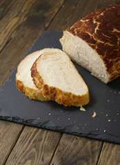 A loaf and slices of crusty white tiger bread on a rustic slate and wooden table top background