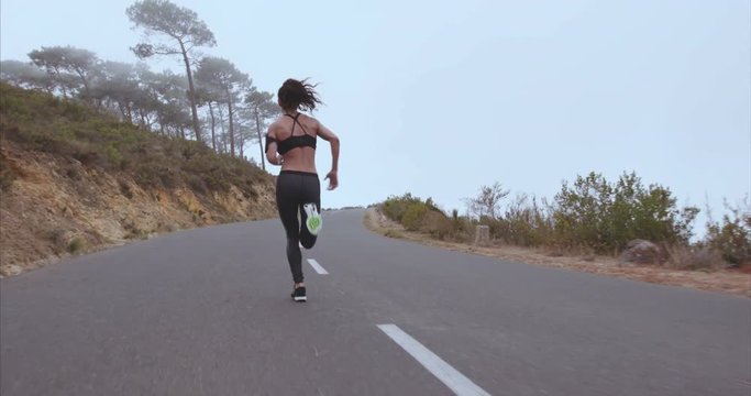 Young female athlete in sportswear taking break from running on the road in morning. Fitness woman in sportwear during outdoor running session.
