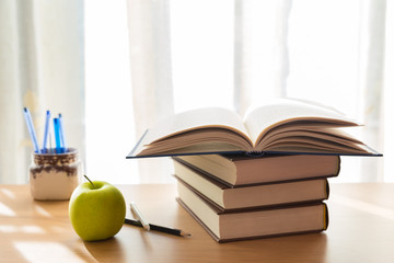Libro aperto sopra libri impilati su tavolo con mela, matite e penne in contenitore portapenne