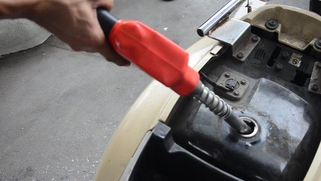 Thai people use gas pump nozzle filling gasoline fuel to tank of motorcycle in oil station at Nonthaburi, Thailand