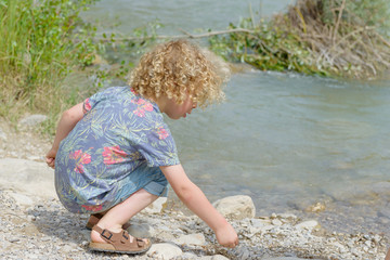 little boy with blond hair plays the waterside