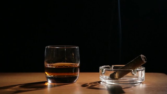Glass of whiskey with smoking cigar.Glass of alcohol and smoking noble cigar on a black background.