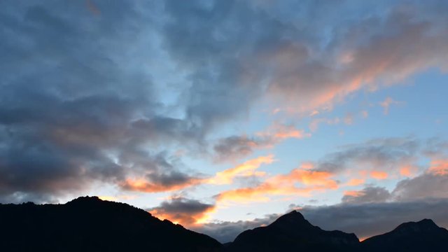 Magnificent panorama of mountains in central Switzerland. Setting sun painted the clouds in the grand color. Wide lens, time lapse.