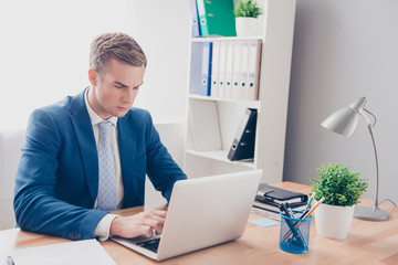 Concentrated young businessmn in blue suit working with laptop