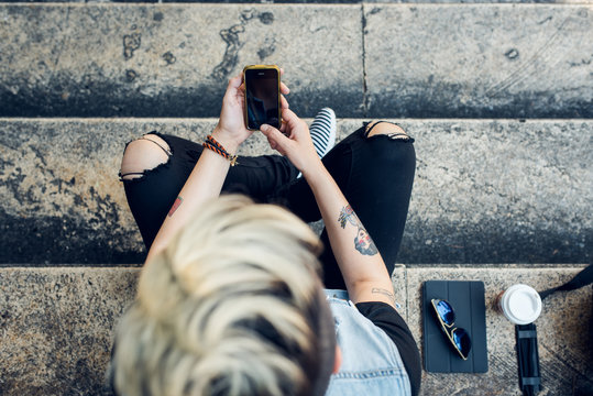 An upper view of stylish young woman using her cell phone while sitting on stairs in the city.
