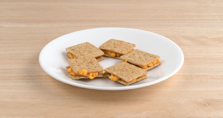 Cheese filled crackers on a white plate side view atop a wood table.