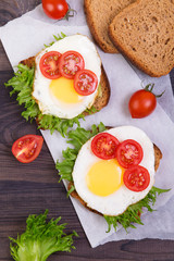 Two sandwiches with egg, lettuce and tomato on a crispy slice of rye bread on a dark wooden background