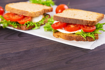 Two homemade sandwich with egg, salad and tomatoes on crispy slice of rye bread on a dark wooden background