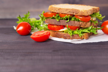 Sandwich with egg, salad and tomatoes on crispy slice of rye bread on a dark wooden background. Space for text
