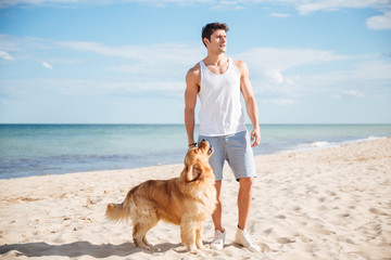 Serious handsome young man with his dog on the beach