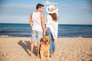 Couple stading and holding hands near their dog on beach