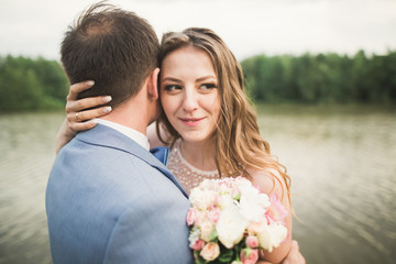 Bride and groom holding beautiful wedding bouquet. Lake, forest