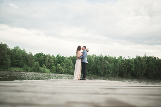 elegant stylish groom with his happy gorgeous brunette bride on the background of a lake