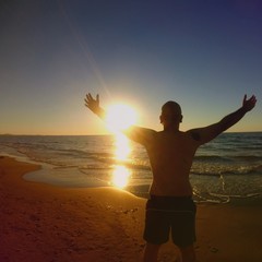 back view of a man with arms up in front of the sea during sunset in sardinia summertime