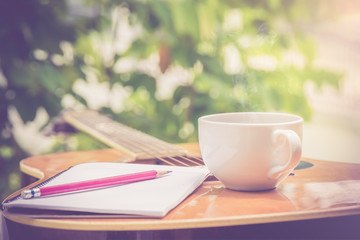 Coffee and Guitar with notebook on blurred nature background for relax time with music Shallow DOF 