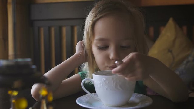 A little kid having breakfast at a cozy cafe. An adorable girl drinking tea and enjoying her breakfast.