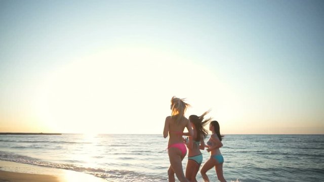 three young female wearing bikini running at the beach slow motion