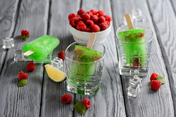 Green Ice Cream Popsicle with Lime and raspberry on a wooden table