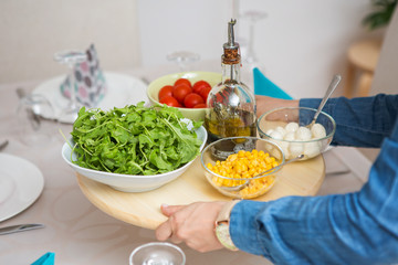 Woman bringing a wooden tray with fresh organic arugula, tomato
