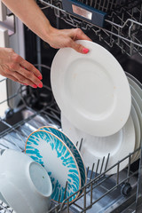 Woman's hand putting a white plate into the dishwasher; a househ
