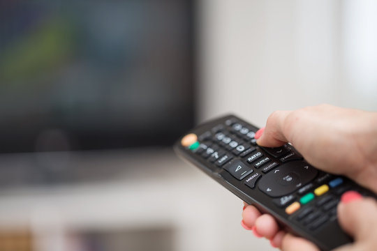 Female hand holding a TV remote control pointed towards the LCD