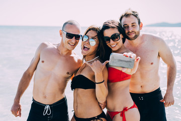 Half length of group of multiethnic friends at the beach in summertime taking selfie in the water, having fun, smiling - friendship, smiling, happiness, vanity, social network concept