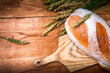 Fresh bread and wheat on wooden background