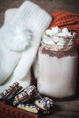 cocoa with marshmallows, chocolate chip cookies, knitted orange scarf and white mittens on wooden background