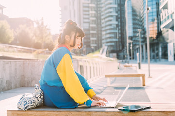 young beautiful asian millennial woman nonconformist outdoor in city back light using computer...