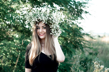 Amazing girl in a black dress and white wreath. Beautiful summer weather. Flowers.