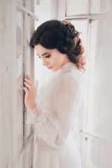 fantasy woman sad Lady in white vintage dress standing in a large castle room white window, fantastic fairy tale princess, trendy historical gown. elegant girl medieval outfit silk clothes dress hair 
